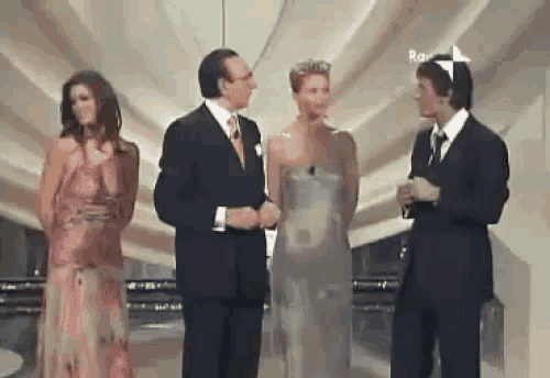 a group of people are standing on a stage and one of them is wearing a pink dress .