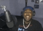 a man wearing headphones and a blue hat is singing into a microphone .