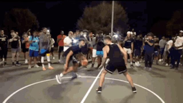 two men are playing basketball on a court at night with a crowd watching