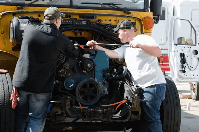 two men are working on the engine of a truck and one has a wrench in his hand