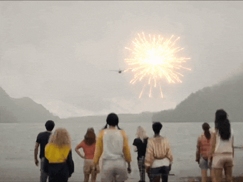 a group of people are watching a fireworks display over a lake