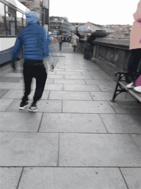 a person in a blue jacket and black pants walking down a sidewalk