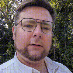 a man with glasses and a beard is wearing a white shirt and looking at the camera .