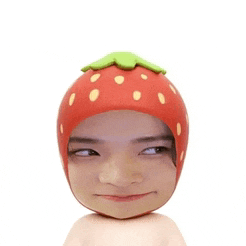 a man wearing a strawberry hat looks at the camera