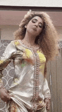a woman with curly hair is wearing a colorful dress and standing in front of a door .