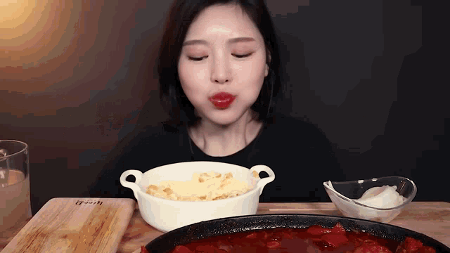 a woman is eating a bowl of food next to a pan of food on a table .