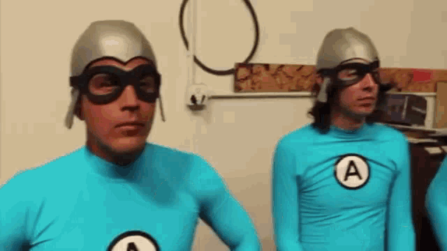 two men in blue superhero costumes with the letter a on their shirt