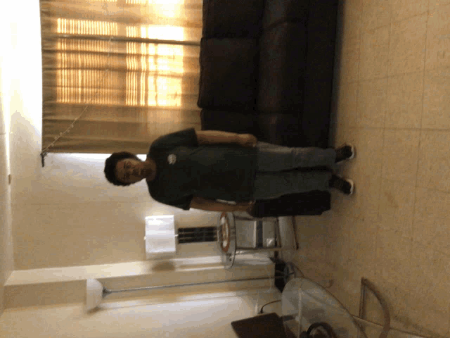 a man in a green shirt stands in a living room with a black couch