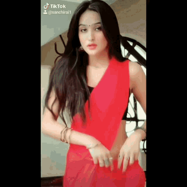 a woman in a red saree is standing in front of a window and looking at the camera .