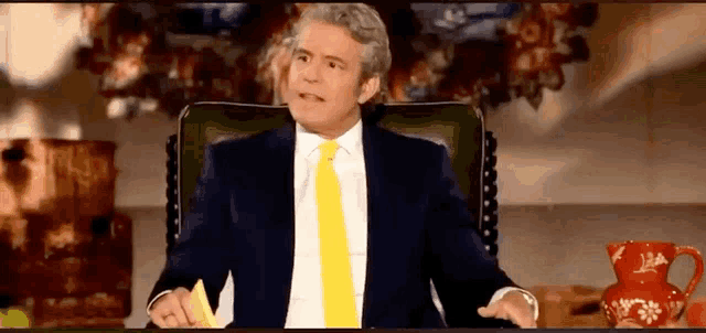 a man in a suit and yellow tie is sitting in a chair holding a piece of paper .