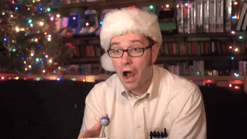 a man wearing glasses and a santa hat holds a blue ball in his hand