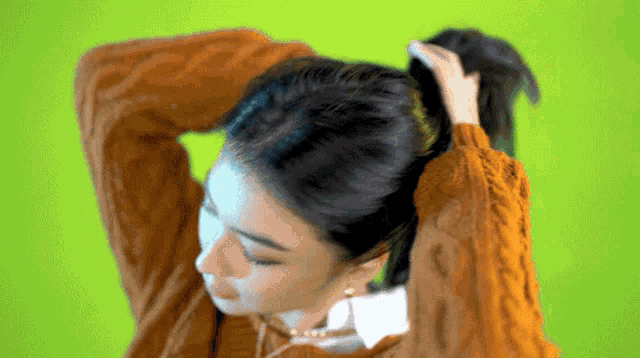 a woman wearing a brown sweater is holding her hair in a ponytail