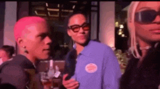 a group of people are standing next to each other at a party . one of the people has pink hair .