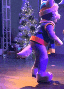 a stuffed animal dancing on a stage with a christmas tree in the background