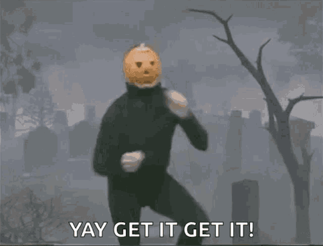 a man with a pumpkin on his head is standing in front of a cemetery .