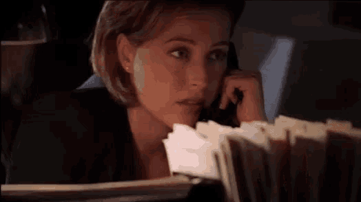 a woman is talking on a phone while looking at a pile of papers
