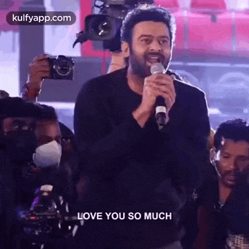 a man is holding a microphone and saying `` i love you so much '' while standing in front of a crowd .