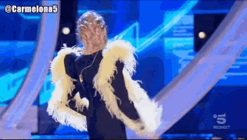 a woman with feathers on her arms is dancing on a stage with the number 5 on the bottom