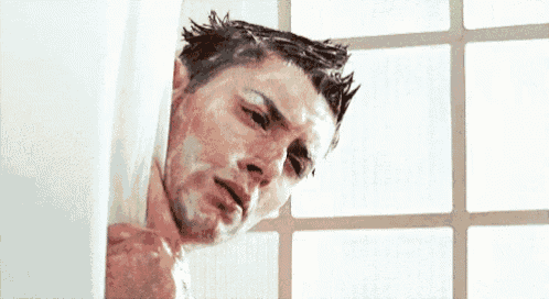 a man is taking a shower in a bathroom and peeking out of the shower curtain .
