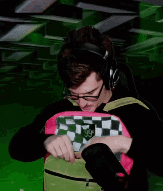 a man wearing headphones and glasses is holding a pink and green checkered backpack that says i love you