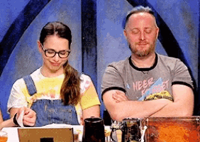 a man and a woman are sitting at a table with their eyes closed and the man is wearing a shirt that says neer