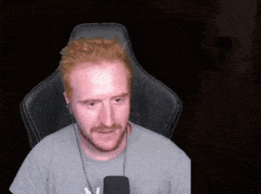 a man with red hair and a beard wearing headphones and a grey shirt with the letter m on it