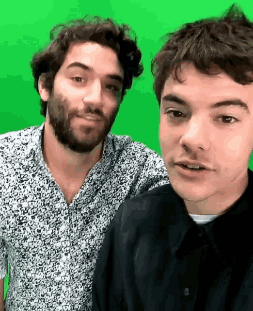 two men are posing for a picture in front of a green background