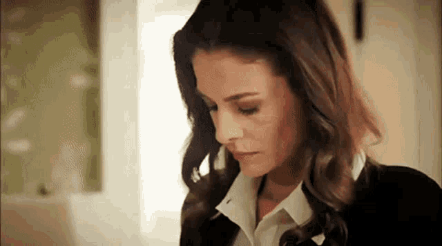 a woman wearing a black jacket and white shirt is looking down .