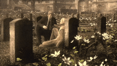 a man kneeling next to a woman laying on the ground in a cemetery