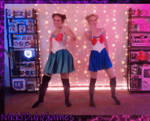 two women in sailor moon costumes are dancing in front of a sign that says nikki dun games