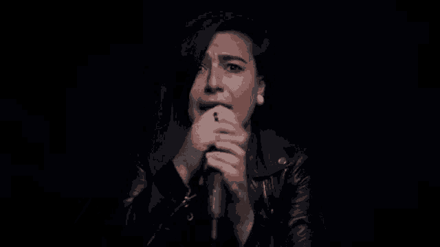 a woman wearing a leather jacket is singing into a microphone .