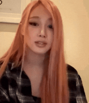 a woman with long red hair is wearing a plaid shirt and making a funny face .