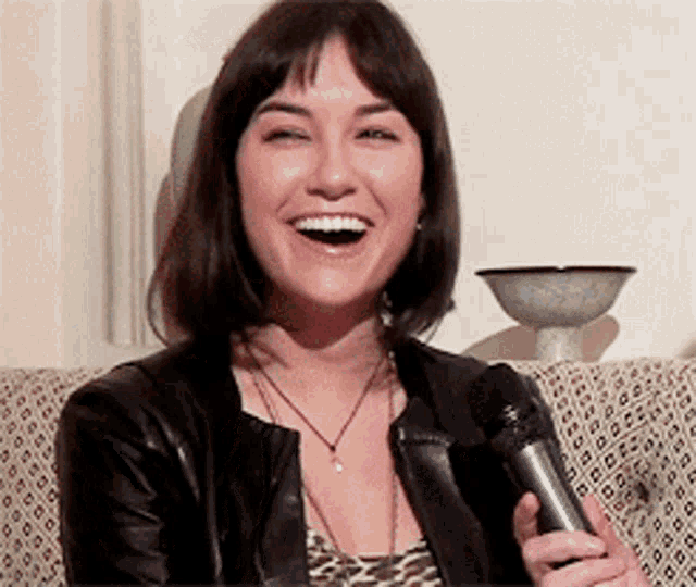 a woman is holding a microphone and smiling while sitting on a couch