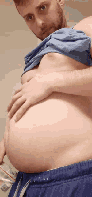 a man with a beard is holding his stomach while wearing blue shorts and a blue shirt .