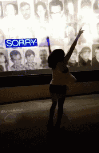 a woman stands in front of a wall with a sign that says sorry