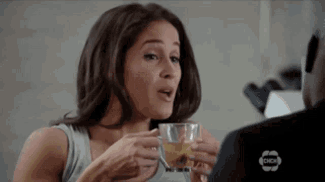 a woman is drinking a cup of tea while talking to a man