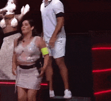 a woman in a white dress is dancing on a stage with a man standing behind her .