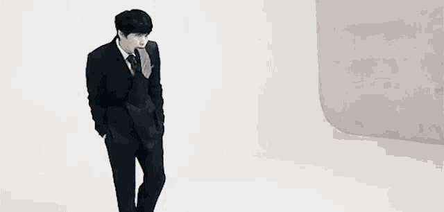 a man in a suit and tie is standing next to a white wall .
