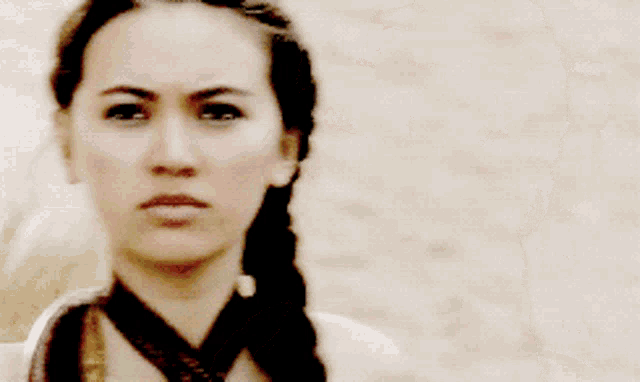 a woman wearing a braided ponytail and a choker looks at the camera