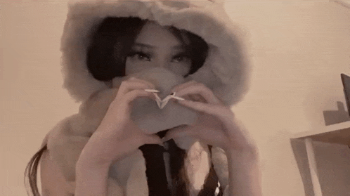 a woman wearing a fur hat is making a heart with her hands .