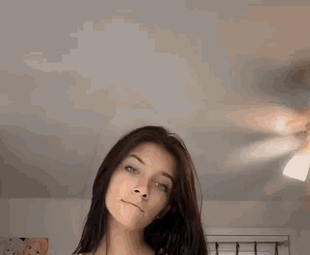 a woman with long dark hair is standing in front of a ceiling fan in a room .