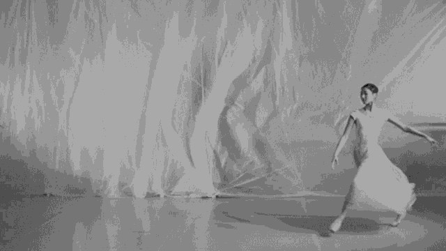 a black and white photo of a ballerina in a white dress dancing on a stage .