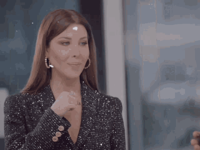 a woman wearing a sequined jacket and hoop earrings is smiling