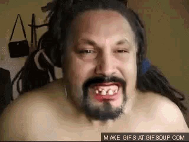 a shirtless man with dreadlocks and a beard is making a funny face while wearing headphones .