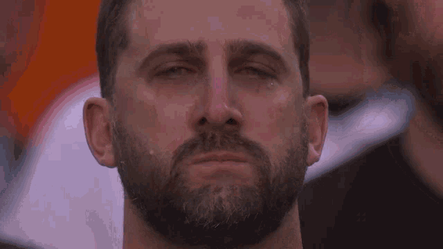 a man with a beard is crying with his eyes closed and a tear running down his face .