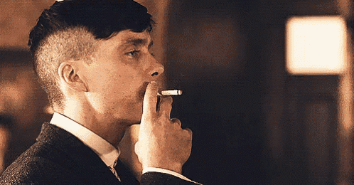 a man in a suit and tie is smoking a cigarette in a room .