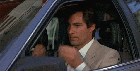 a man in a suit and tie is sitting in a car and making a fist .