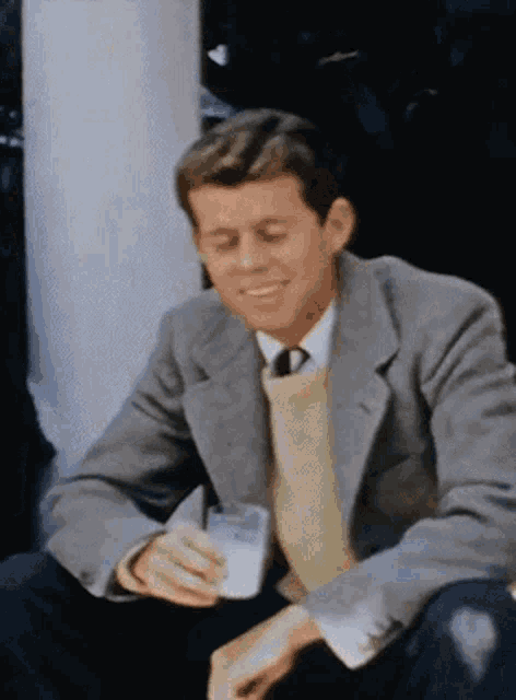 a man in a grey jacket and yellow sweater is drinking a glass of milk