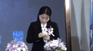a woman in a black suit is holding a bouquet of purple flowers