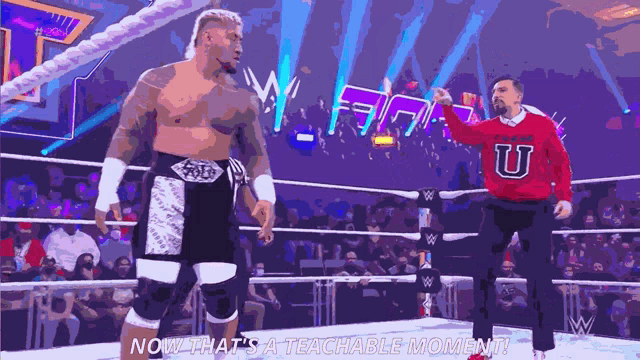 a man in a red sweater with the letter u on it is standing in a wrestling ring